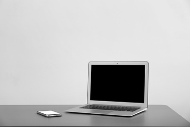 Photo of Modern laptop with blank screen and mobile phone on table against light background