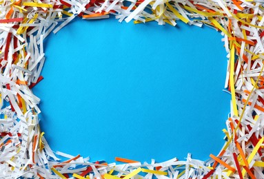 Photo of Frame of shredded colorful paper strips on light blue background, flat lay. Space for text
