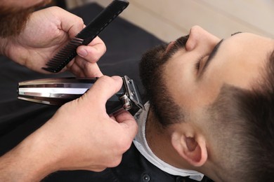 Photo of Professional hairdresser working with client in barbershop, closeup