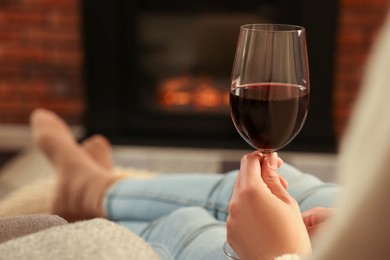 Photo of Woman with glass of wine relaxing near fireplace at home, closeup. Space for text
