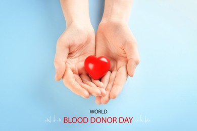 Image of World Blood Donor Day. Woman holding small red heart on light blue background, top view