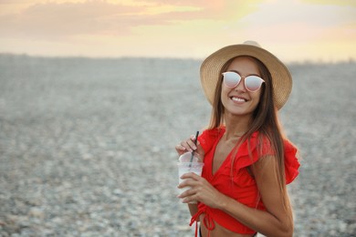 Beautiful young woman with tasty milk shake on beach, space for text