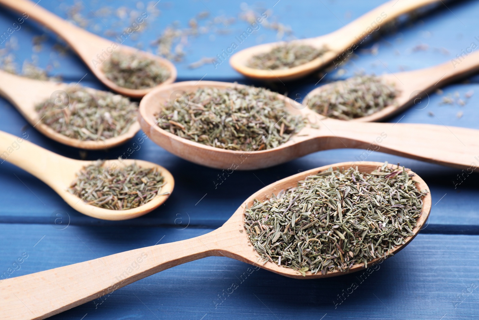 Photo of Spoons with dried thyme on blue wooden table, closeup