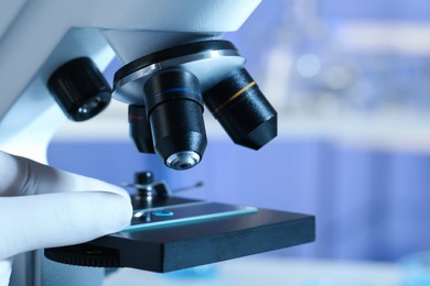 Photo of Scientist examining sample of light blue liquid on slide under microscope in laboratory, closeup