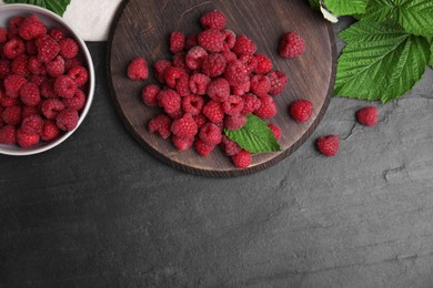 Photo of Fresh ripe raspberries with green leaves on black table, flat lay. Space for text