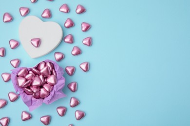 Photo of Box and delicious heart shaped candies on light blue background, flat lay. Space for text