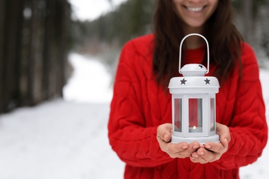 Photo of Woman holding lantern with burning candle near snowy forest. Space for text