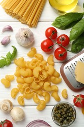 Different types of pasta, grater and products on white wooden table, flat lay