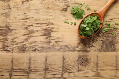 Photo of Cut fresh green cilantro and spoon on wooden table, flat lay. Space for text