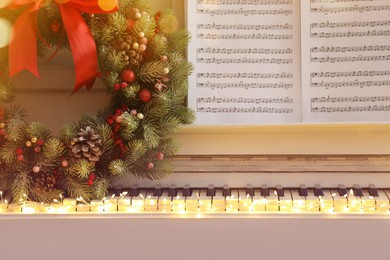Photo of White piano with decorative wreath and note sheets closeup. Christmas music