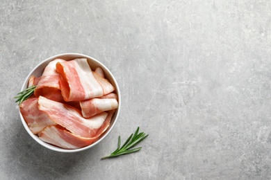 Photo of Bowl with raw bacon rashers on grey background