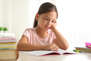 Photo of Sad little girl doing homework at table indoors