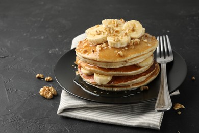 Photo of Delicious pancakes with bananas, walnuts and honey on dark textured table, closeup. Space for text