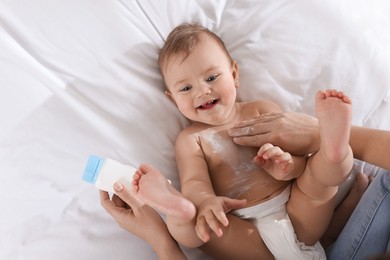 Photo of Mother applying dusting powder onto her baby on bed, top view