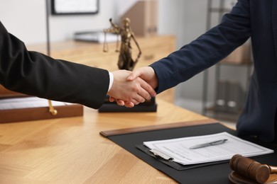 Photo of Notary shaking hands with client at wooden table in office, closeup