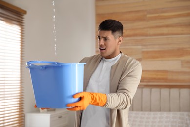 Photo of Emotional man collecting water leaking from ceiling in bedroom. Damaged roof