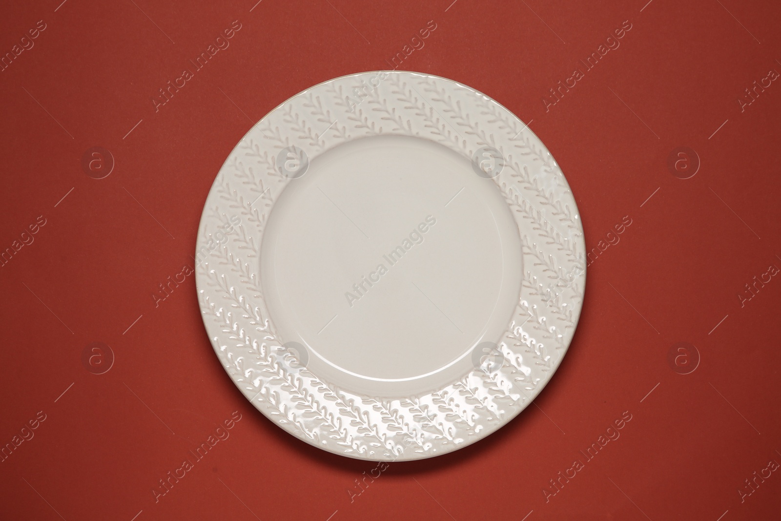 Photo of One white plate on red background, top view