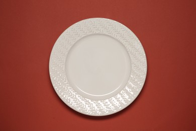 Photo of One white plate on red background, top view