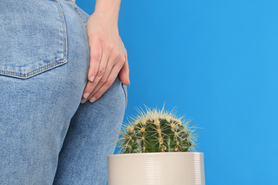 Photo of Woman sitting down on cactus against light blue background, space for text. Hemorrhoid concept