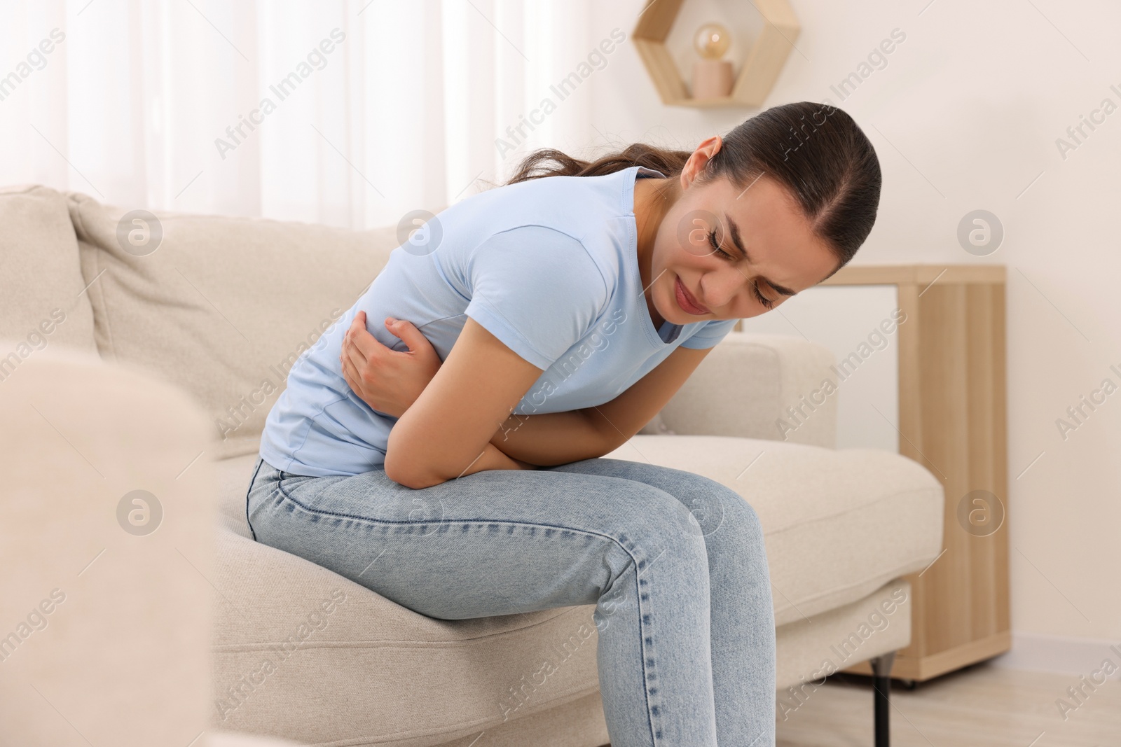 Photo of Woman suffering from abdominal pain on sofa at home. Unhealthy stomach