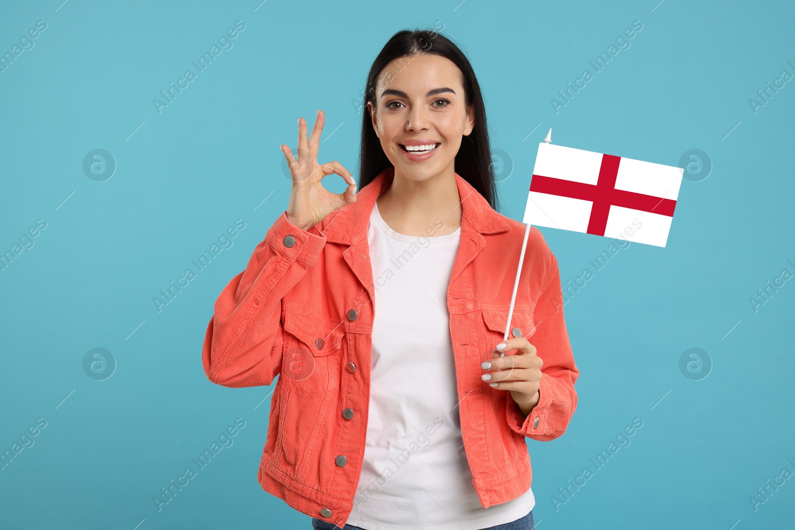 Image of Happy young woman with flag of England showing OK gesture on light blue background