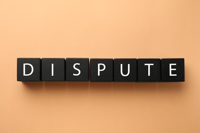 Photo of Black cubes with word Dispute on pale orange background, top view