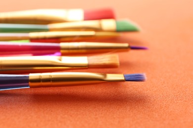 Photo of Set of different paintbrushes on orange background, closeup