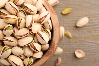 Photo of Tasty pistachios in bowl on wooden table, top view. Space for text