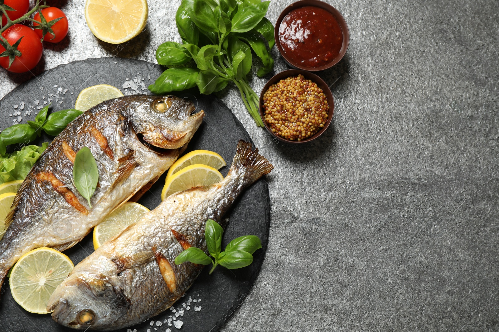 Photo of Delicious roasted fish with lemon on grey table, flat lay. Space for text