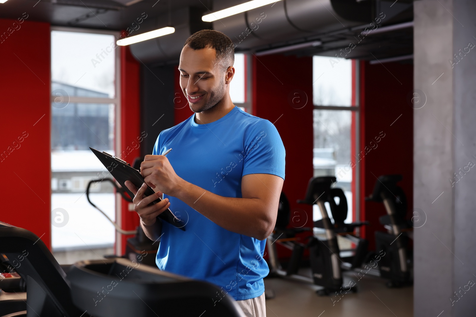 Photo of Happy trainer writing down workout plan in modern gym, space for text