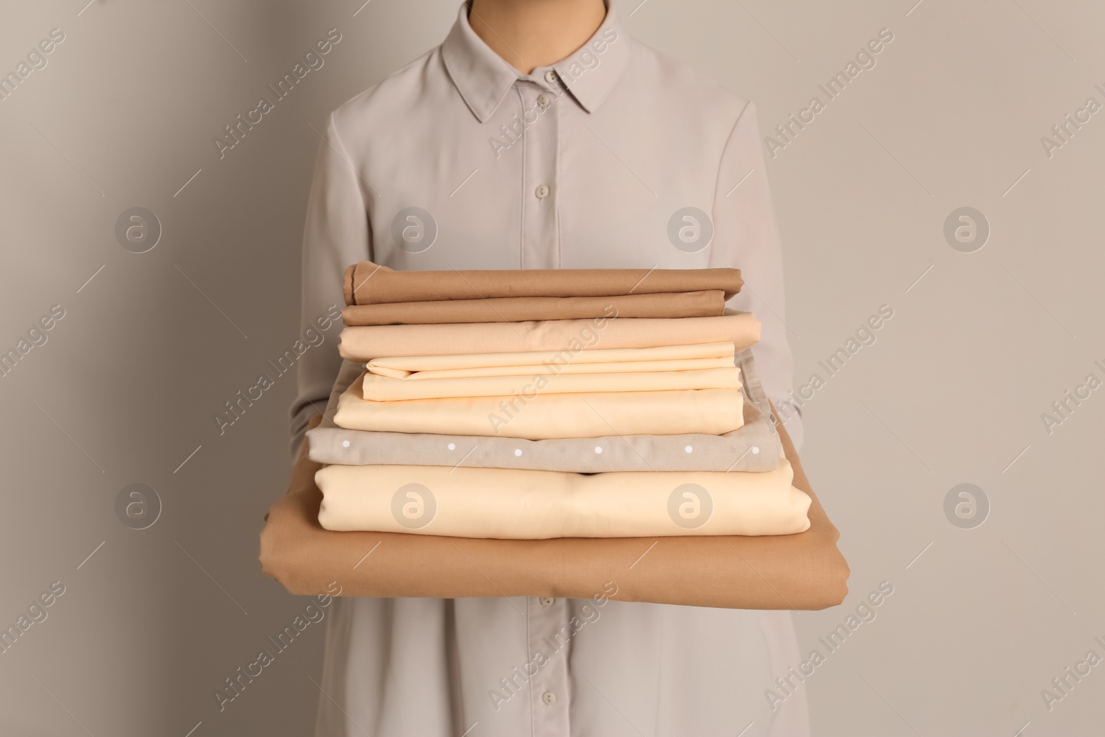 Photo of Woman holding stack of clean bed linens on beige background