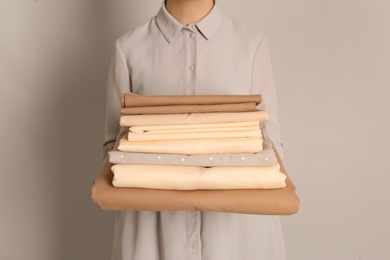 Woman holding stack of clean bed linens on beige background