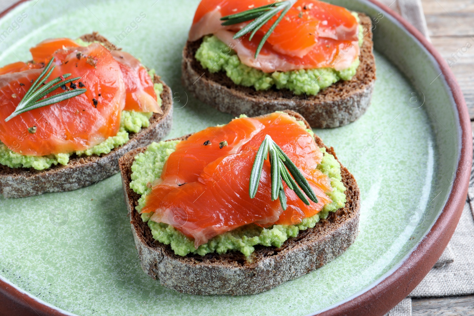 Photo of Delicious sandwiches with salmon, avocado and rosemary on plate, closeup