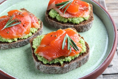 Delicious sandwiches with salmon, avocado and rosemary on plate, closeup