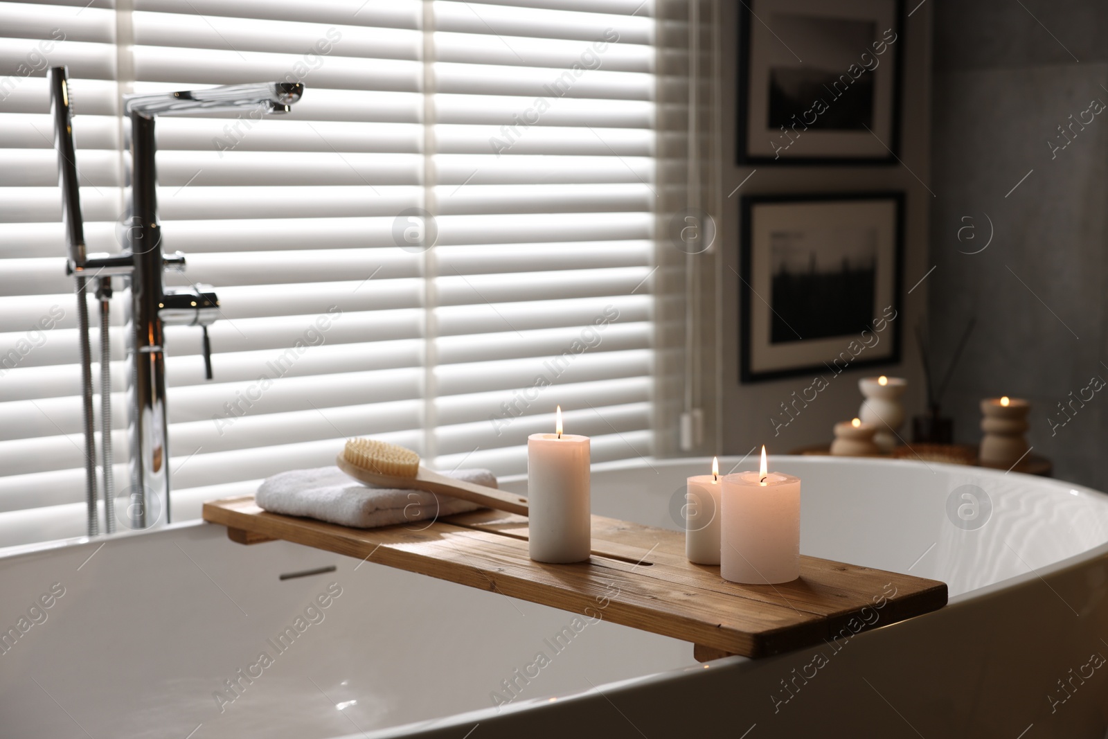 Photo of Wooden tray with burning candles, towel and brush on bathtub in bathroom