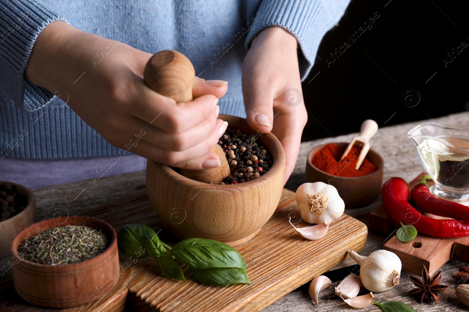 Photo of Woman grinding peppercorns at wooden table, closeup