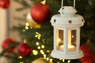 Photo of Christmas lantern with burning candle on fir tree against blurred background, closeup. Space for text