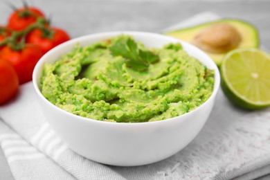 Photo of Bowl of delicious guacamole and ingredients on cloth, closeup