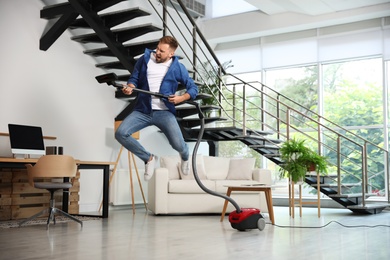 Photo of Young man having fun while vacuuming in living room