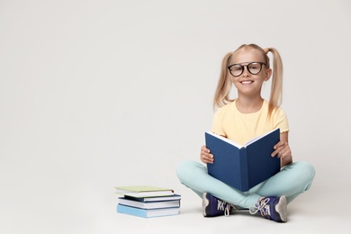 Photo of Cute little girl with glasses reading book on grey background. Space for text