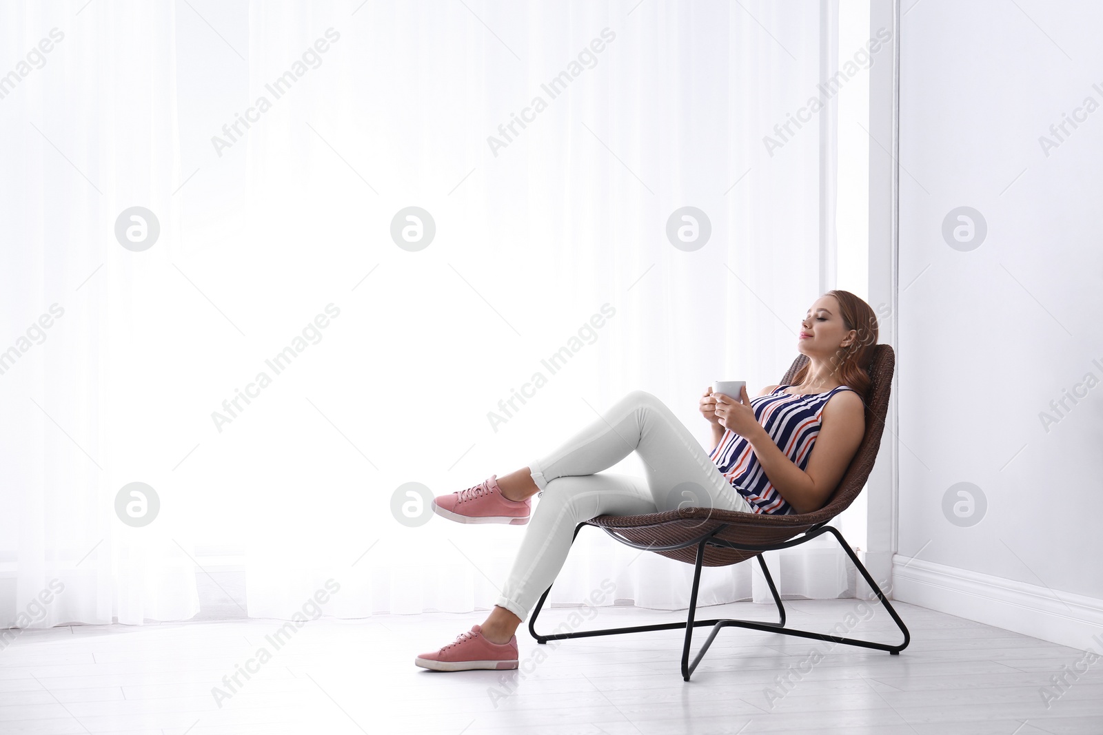 Photo of Young woman with cup of hot drink sitting in armchair at home. Space for text