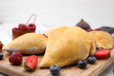 Wooden board with delicious samosas and berries on table, closeup