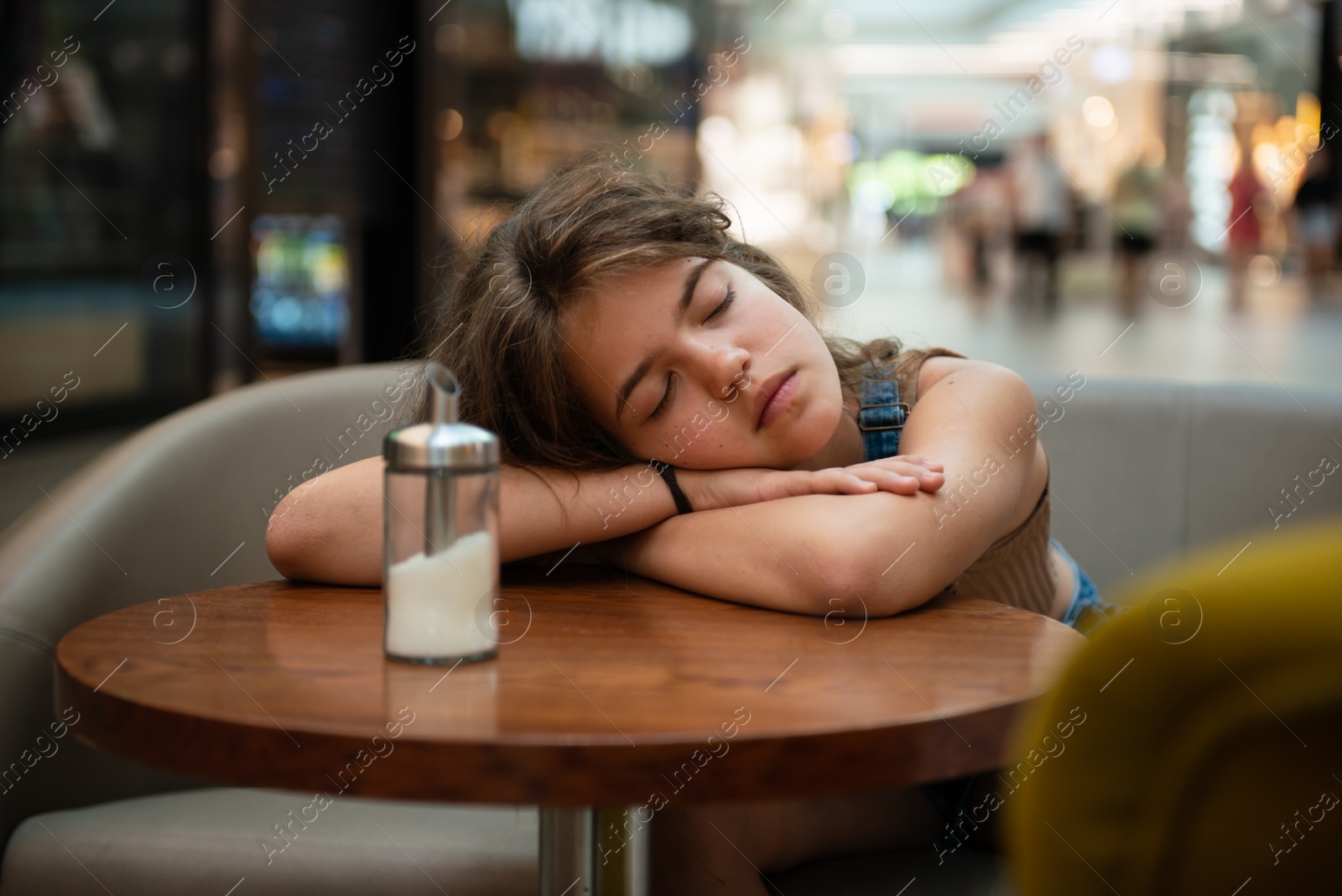 Photo of Tired teenage girl sleeping on wooden table in cafe