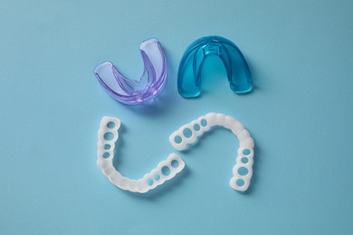 Different dental mouth guards on light blue background, flat lay. Bite correction