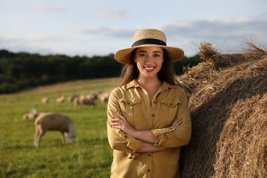 Smiling woman near hay bale on animal farm. Space for text