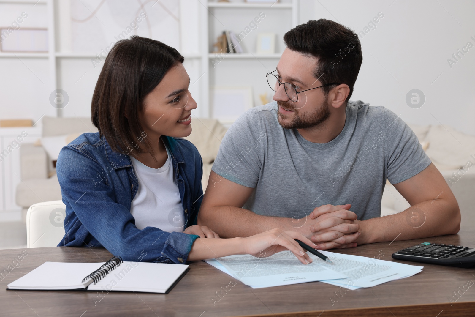 Photo of Young couple with papers discussing pension plan at wooden table indoors