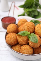 Photo of Bowl of delicious fried tofu balls with basil on white wooden table, closeup
