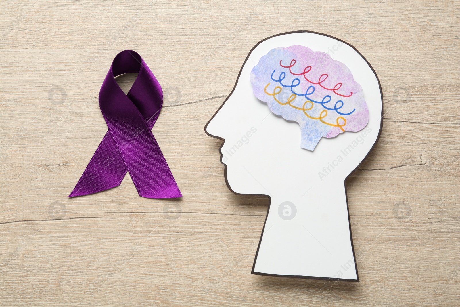 Photo of Human head cutout with brain near purple ribbon on wooden table, flat lay. Epilepsy awareness