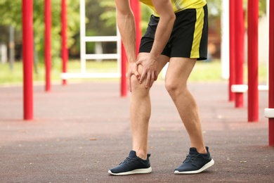 Young man suffering from knee pain on sports ground, closeup