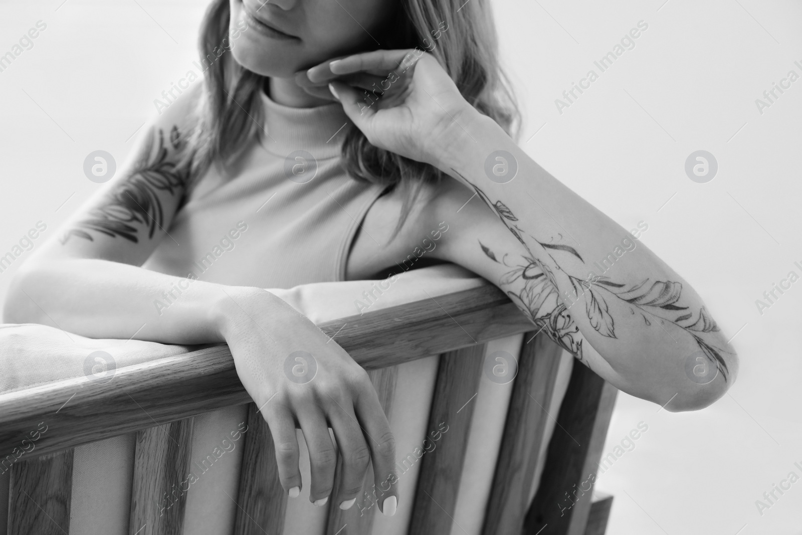 Image of Beautiful woman with tattoos on arms resting indoors, closeup. Black and white photography